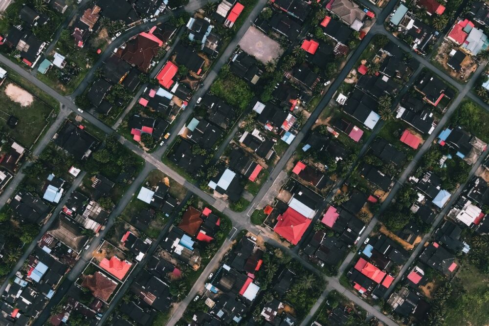 Aerial view of a dense tropical landed neighbourhood with red and grey rooftops and green trees